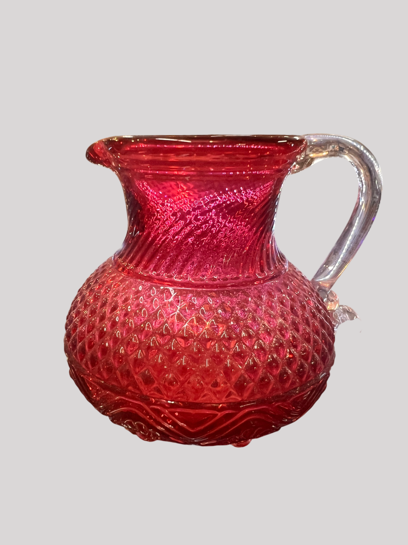 Small hand-blown ruby red art glass pitcher with diamond quilted pattern, clear applied handle, and pontil scar. Likely mid–20th century studio or decorative art glass