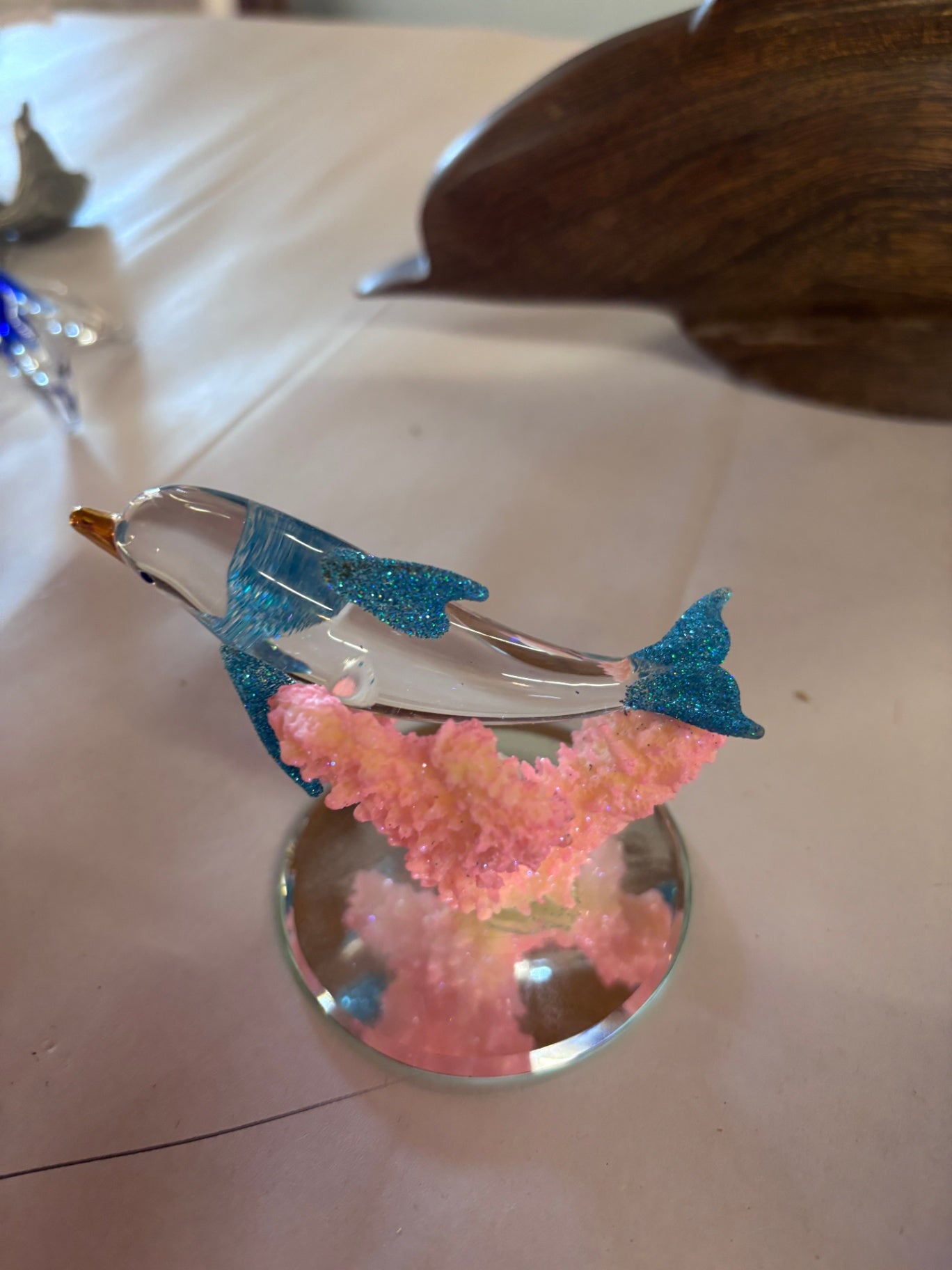 Decorative hand-blown art glass dolphin figurine featuring blue glitter accents on the fins and tail, mounted on a pink coral-like base.