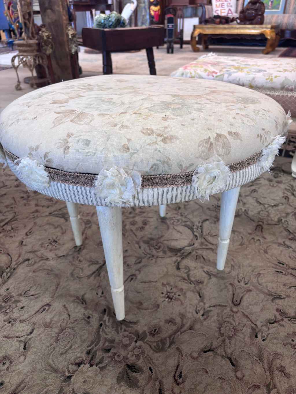 Swivel footstool featuring a floral upholstered seat, off-white painted legs, and decorative fabric rosette trim