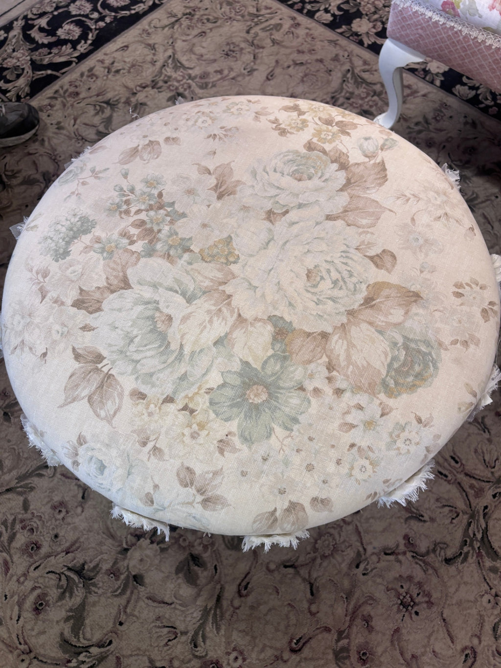 Swivel footstool featuring a floral upholstered seat, off-white painted legs, and decorative fabric rosette trim