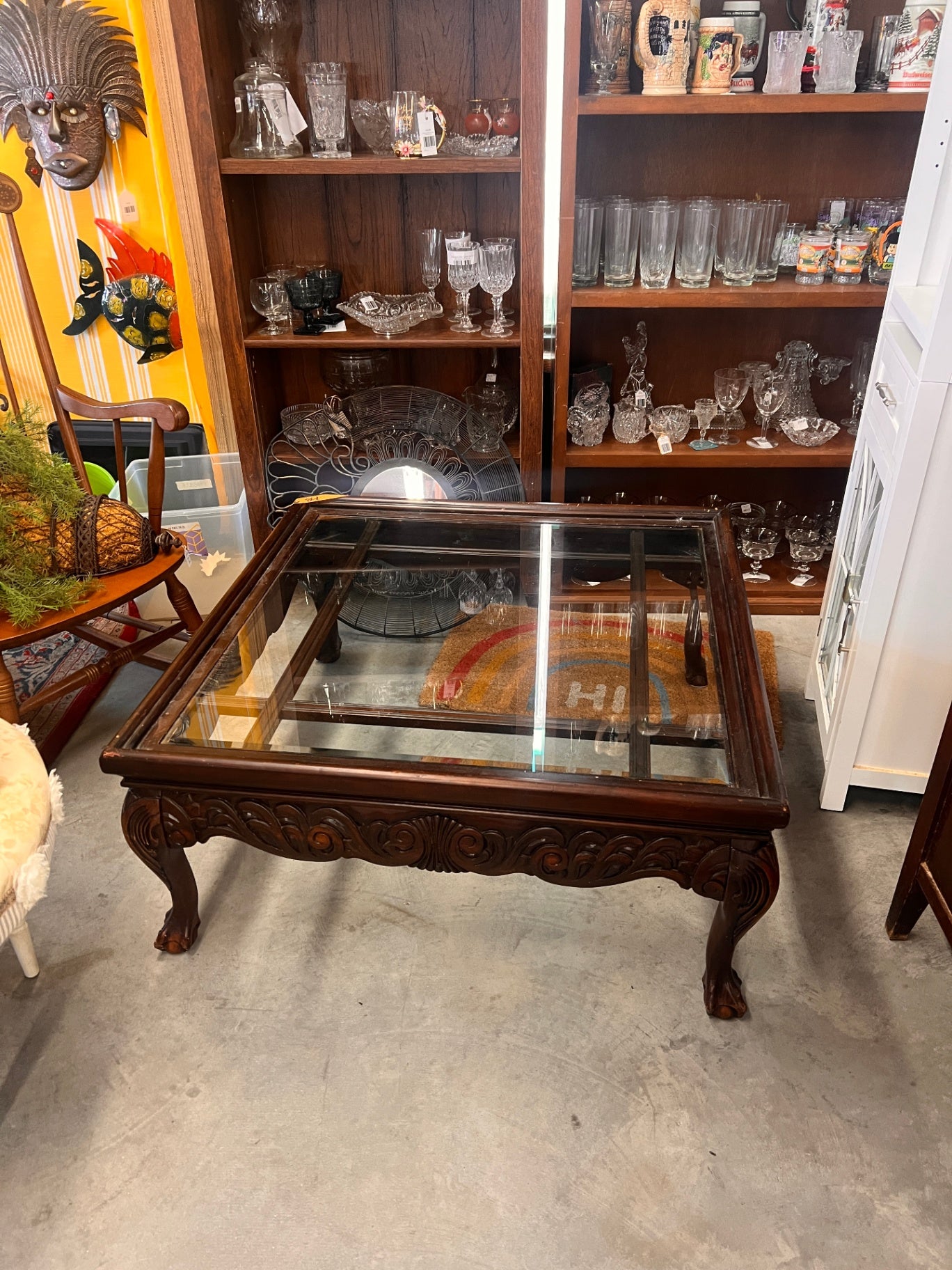 This is a carved mahogany and glass cocktail table, which features a solid wood frame with intricate carvings and a glass top. 