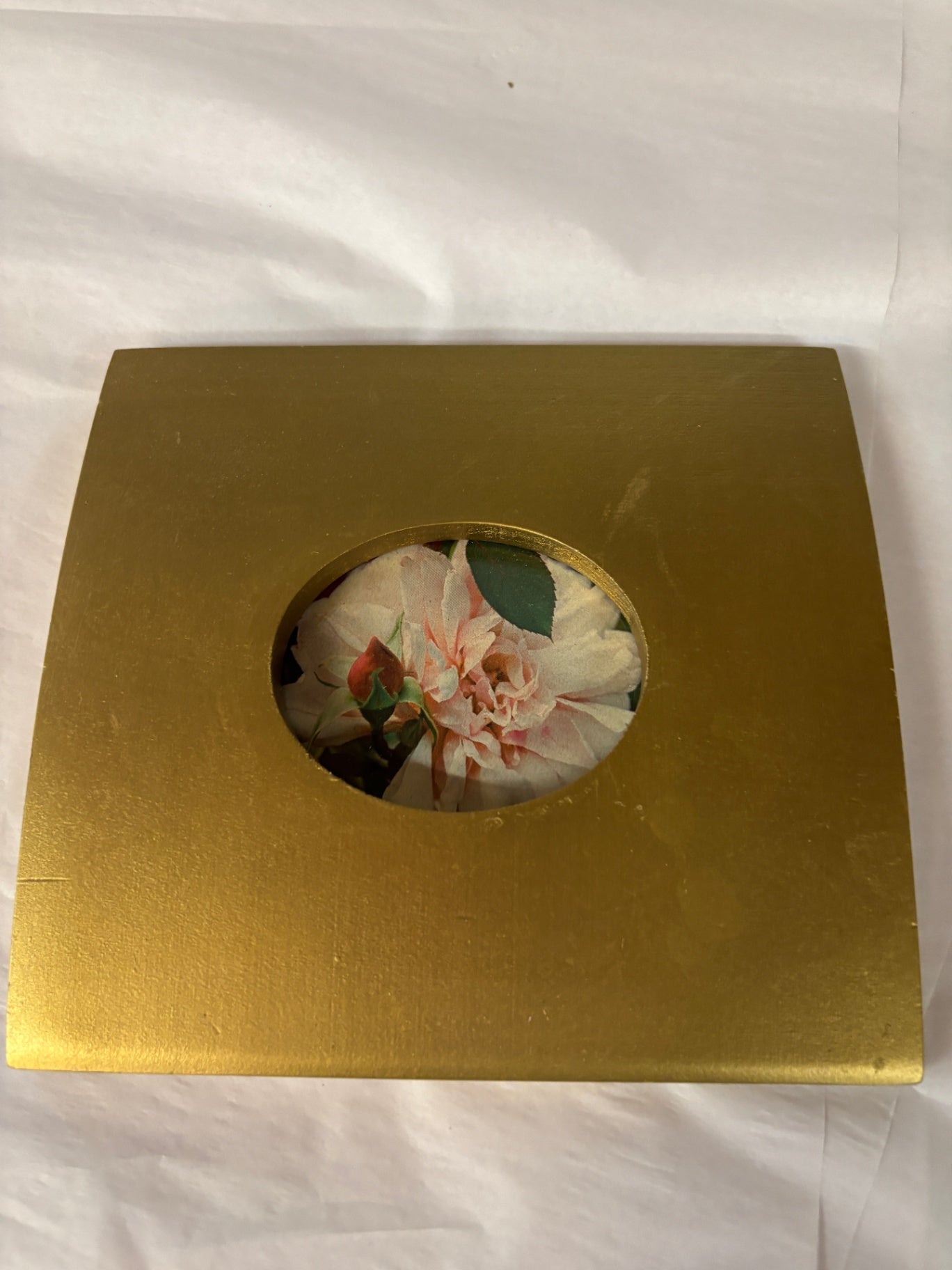 This gold-toned picture frame features a square design with a circular cutout displaying a floral photograph.