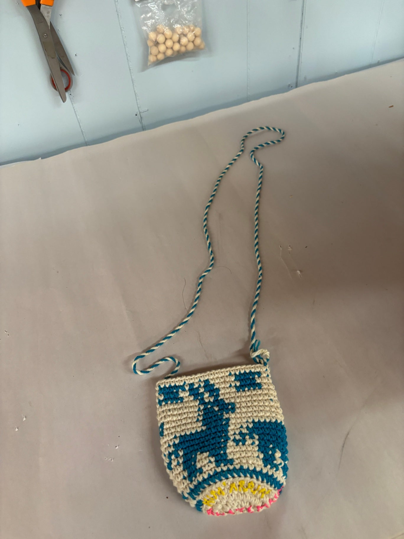 This artisanal cream and blue crocheted bag features a tapestry-style animal motif