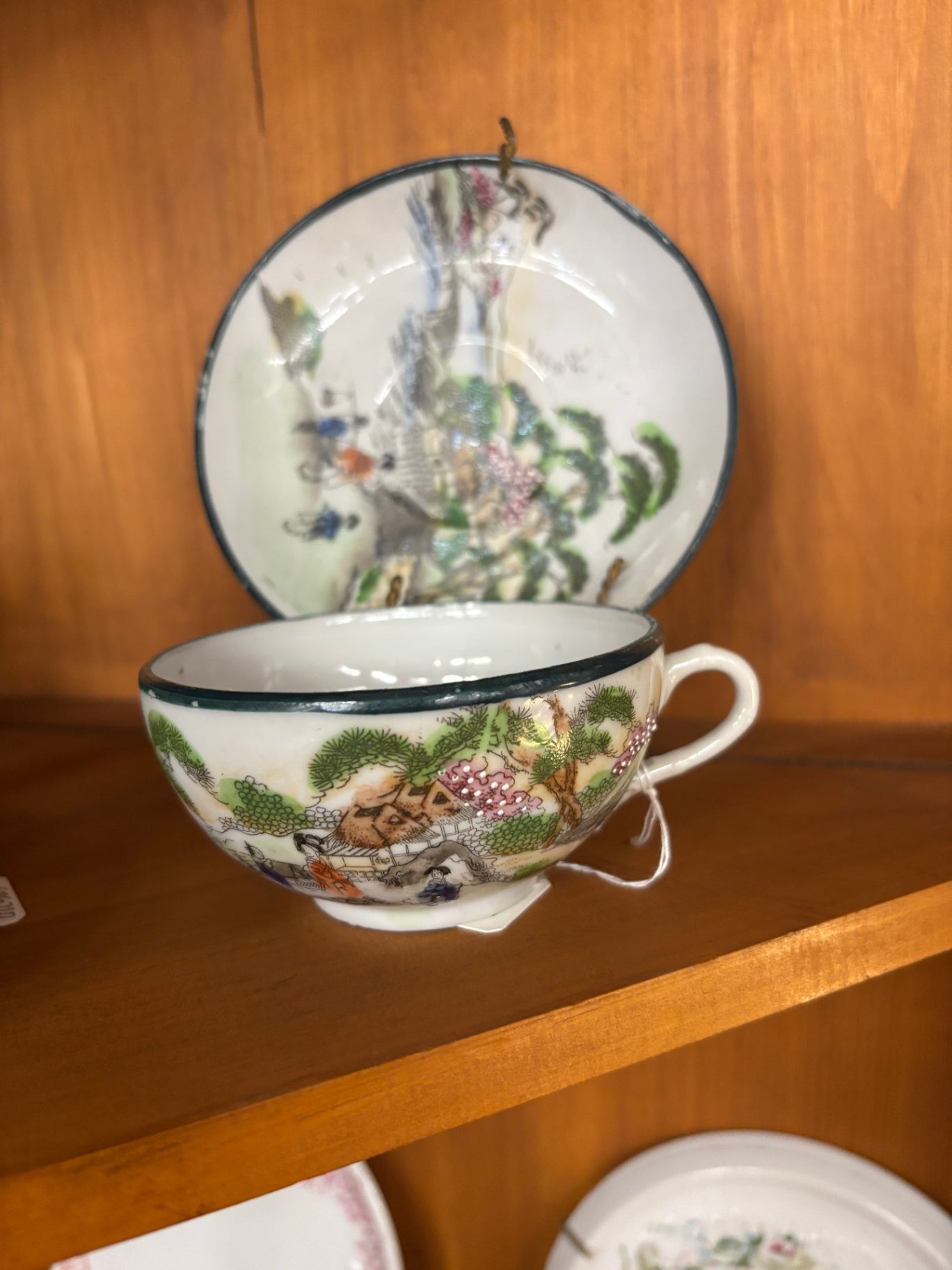 Japanese tea cup and saucer set likely dates from the Mid-Century era and features hand-painted scenes of a Japanese garden or village