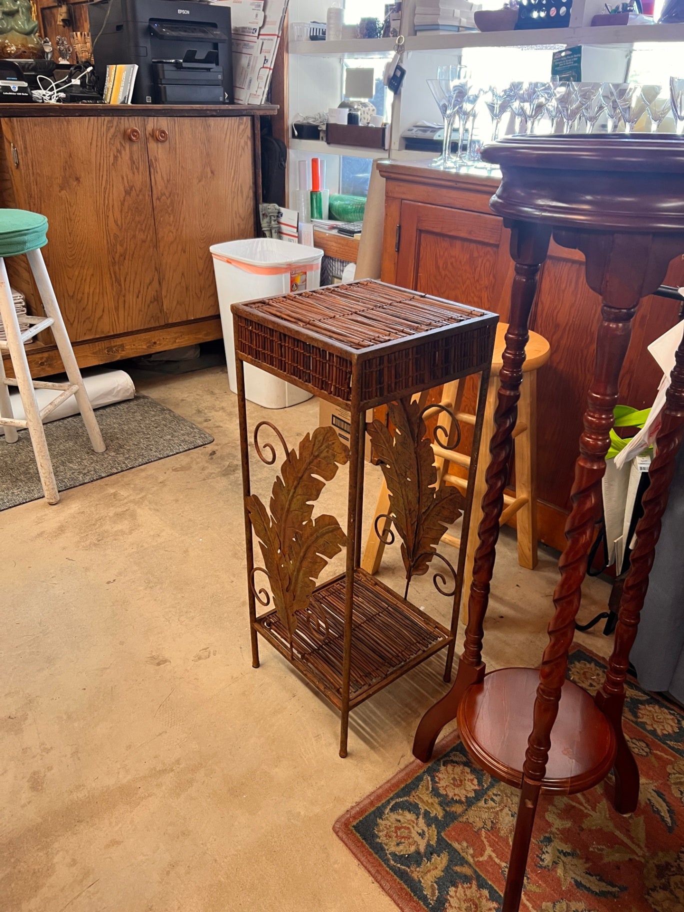 This plant stand features decorative brown metal leaves and a woven rattan top and bottom shelf.