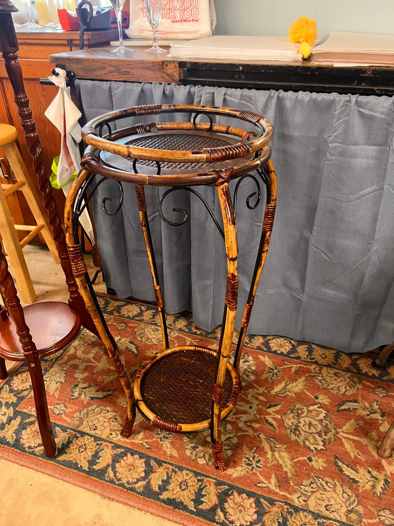 This is a two-tiered Mediterranean Riviera-style plant stand featuring burnt rattan and hand-forged iron scrollwork.