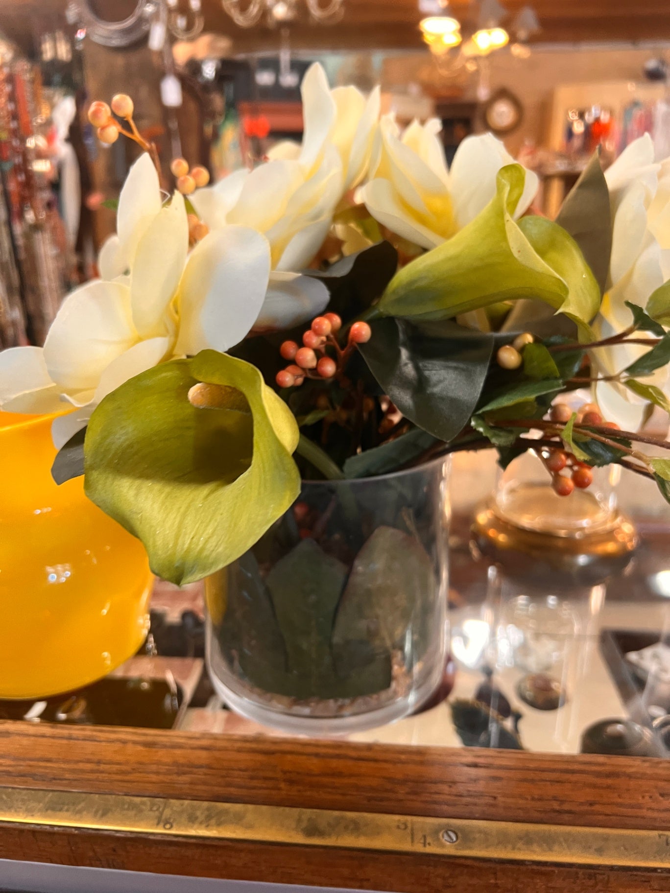 This artificial flower arrangement features cream-colored and green calla lilies housed in a clear glass vase