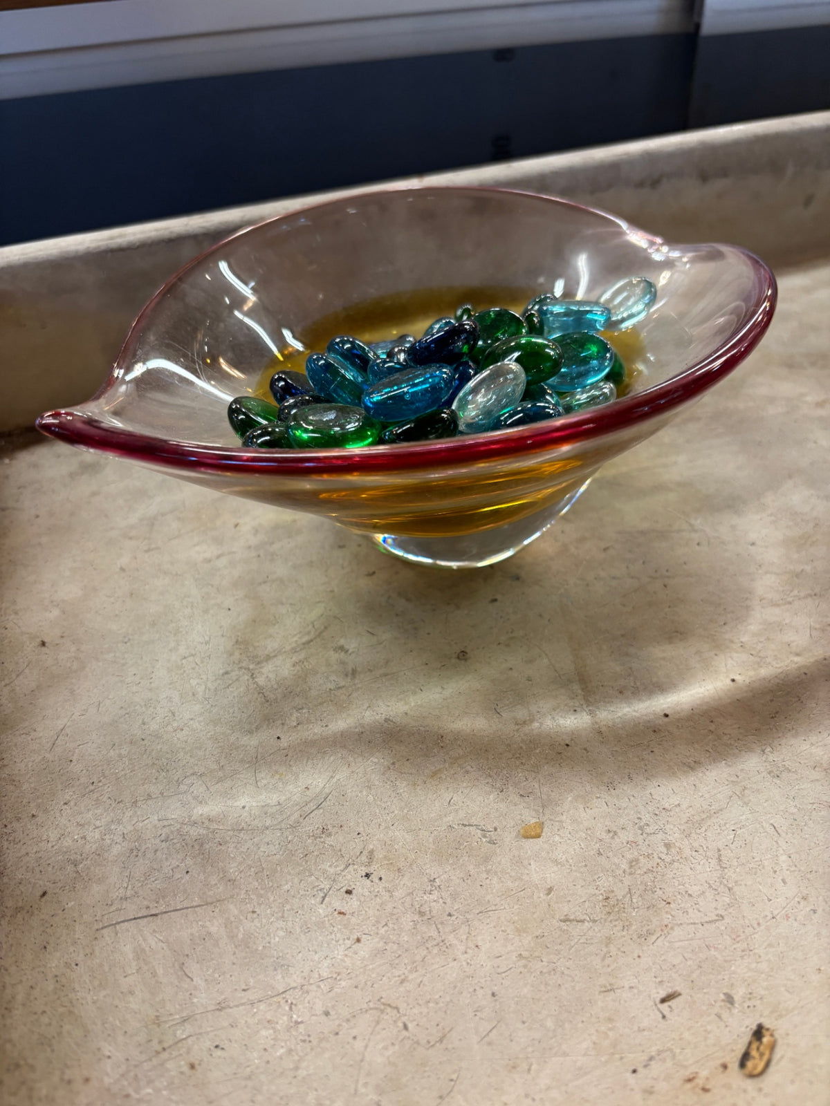 Amber and clear art glass bowl filled with blue and green flat glass gemstones