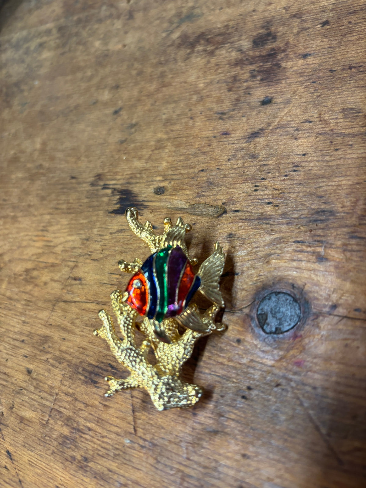 charming vintage brooch features a tropical fish with vibrant red, green, and purple enamel stripes nestled among textured gold-tone coral