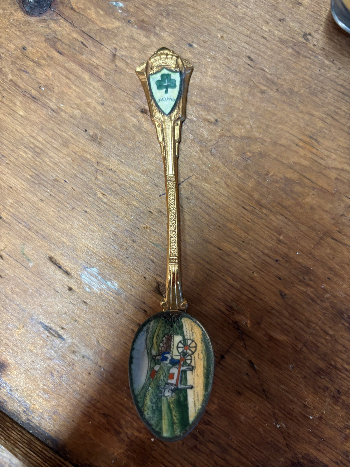 vintage gold-tone souvenir spoon from Ireland featuring an enameled shamrock crest on the handle and a painted pastoral or horse-drawn cart scene inside the bowl