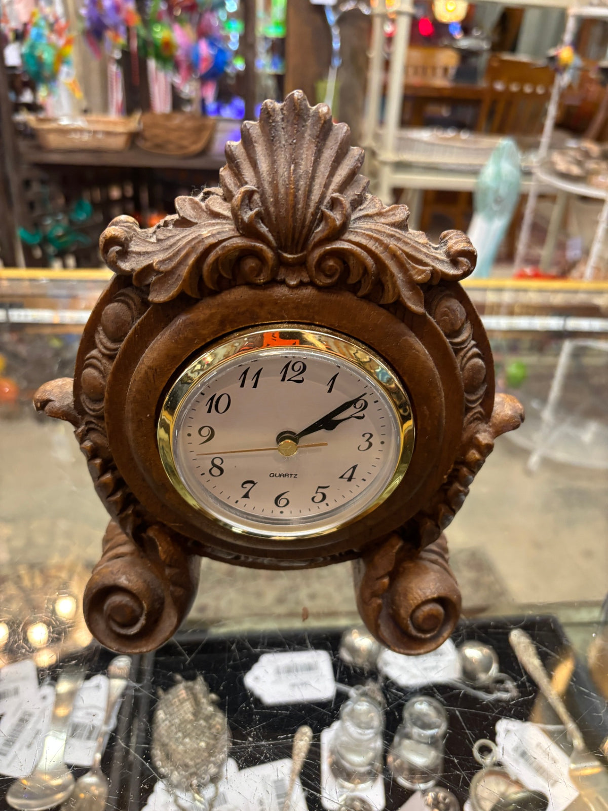 Decorative tabletop or mantel clock featuring an elaborate Baroque-inspired design with a scalloped shell crest, scrolling acanthus leaves, and curled feet.