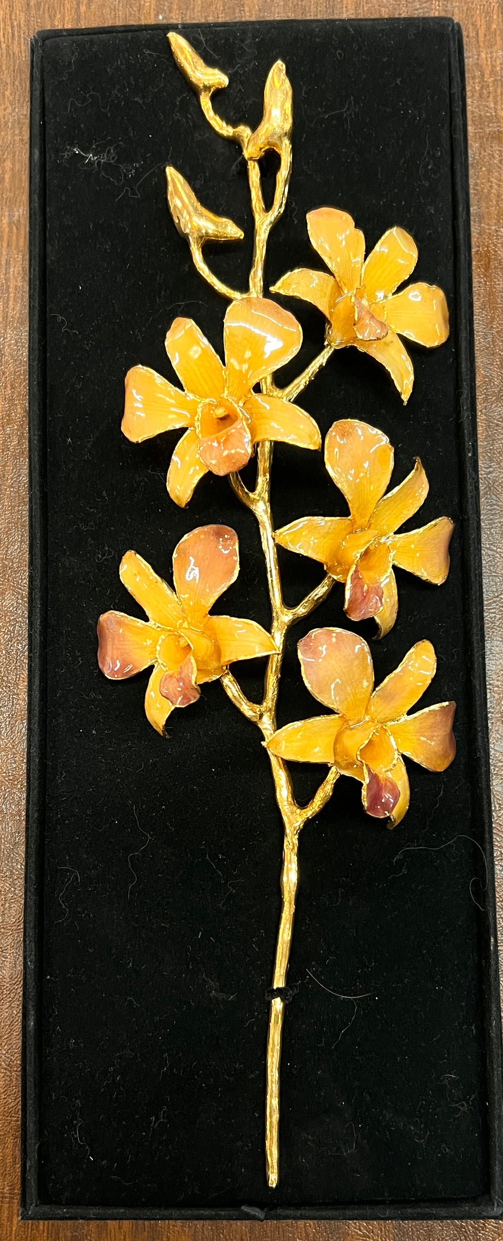 Gold floral hairpin on a black display stand against a wooden background