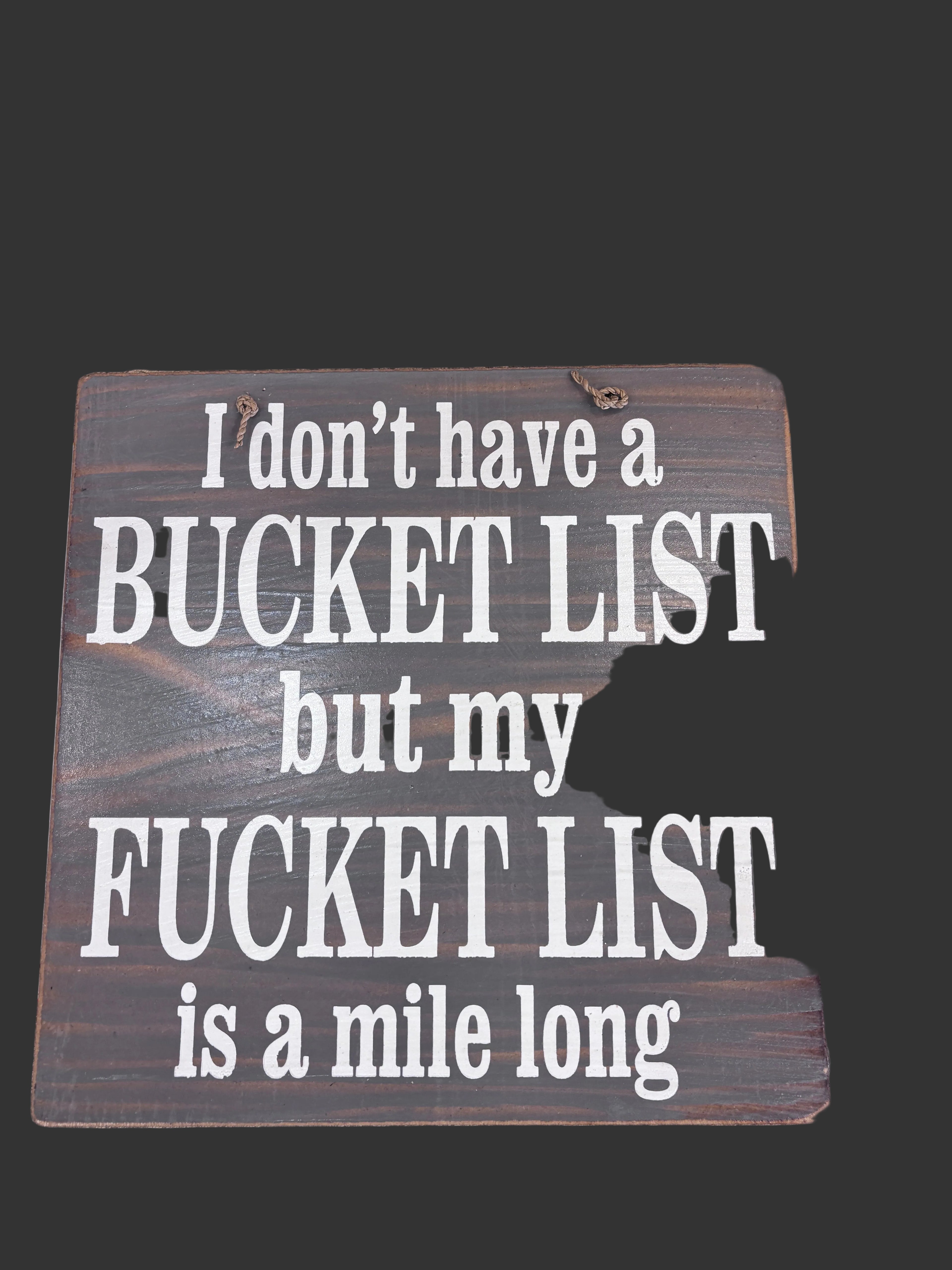 A rustic rectangular wooden sign with white text that reads, 'I don't have a BUCKET LIST but my *UCKET LIST is a mile long,.