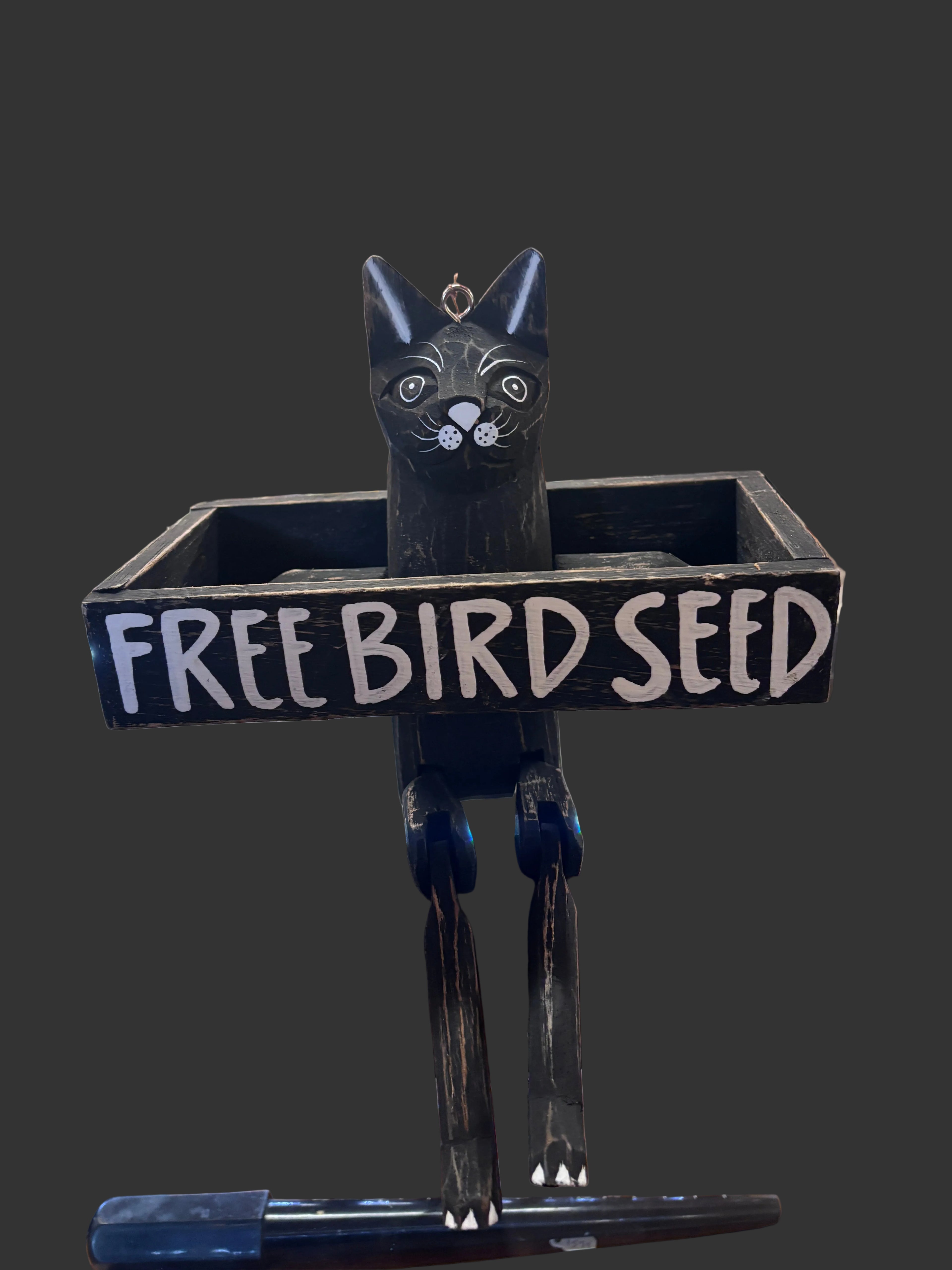 A black bird seed hopper shaped like a cat with a vertical sign reading 'FREE BIRD SEED' in white letters,
