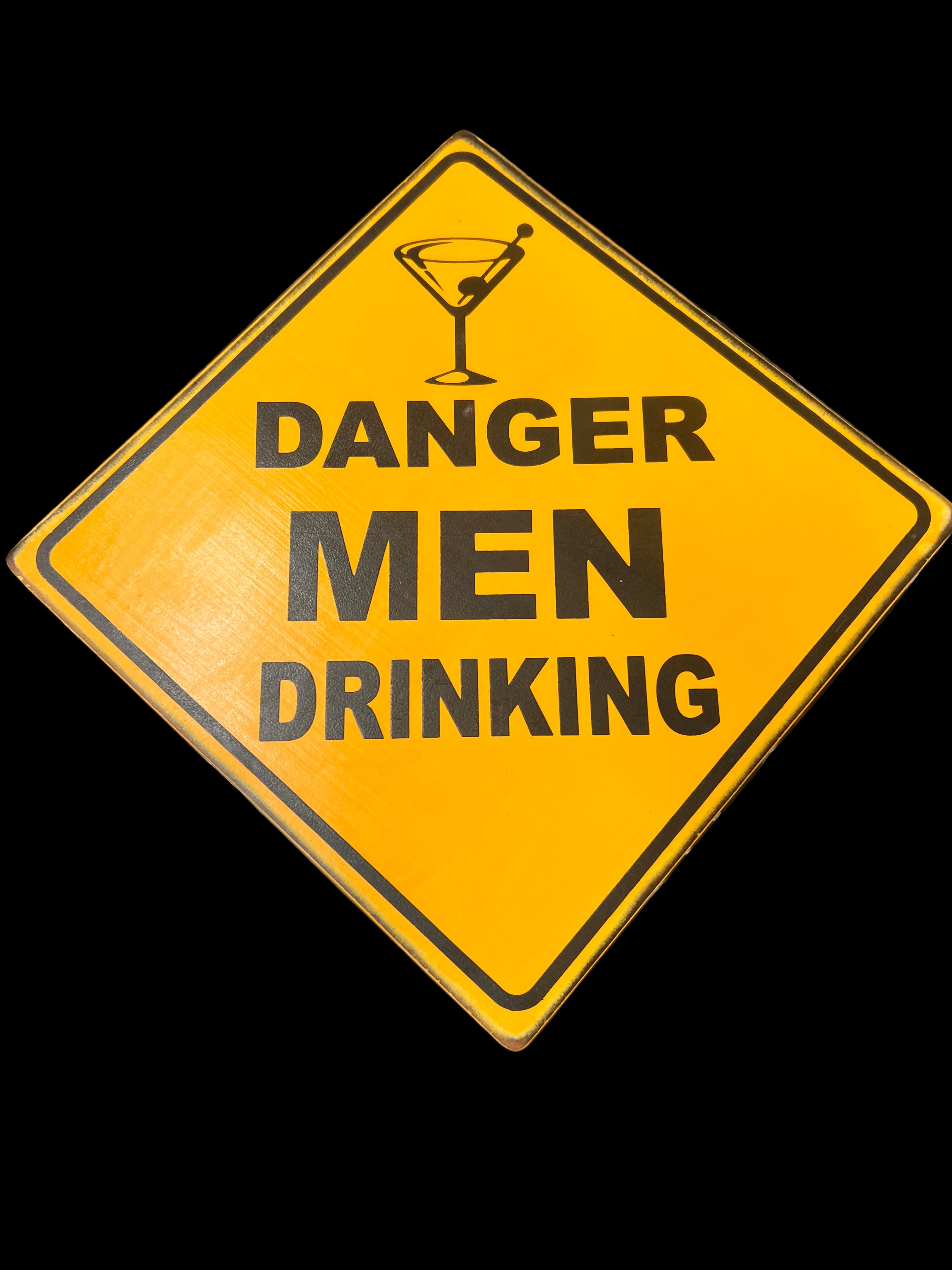 Yellow warning sign with 'Danger Men Drinking' text and a cocktail glass icon on a reflective surface.
